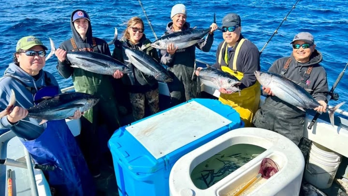Group of six people on a boat holding freshly caught fish over the ocean.