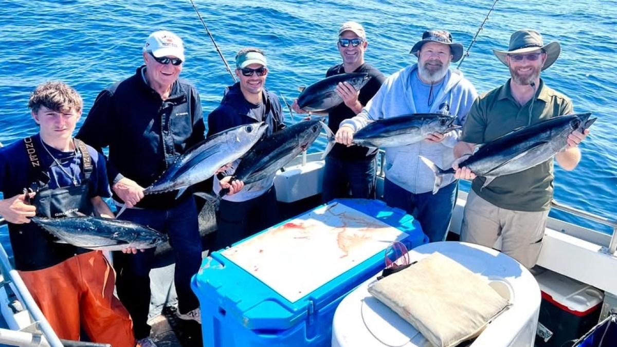 Six people on a boat holding caught fish with blue ocean as background.