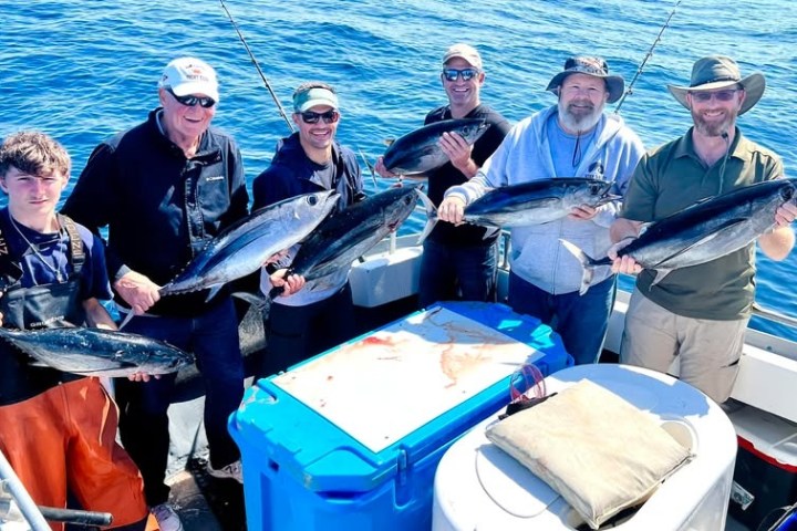 Six people on a boat holding caught fish with blue ocean as background.