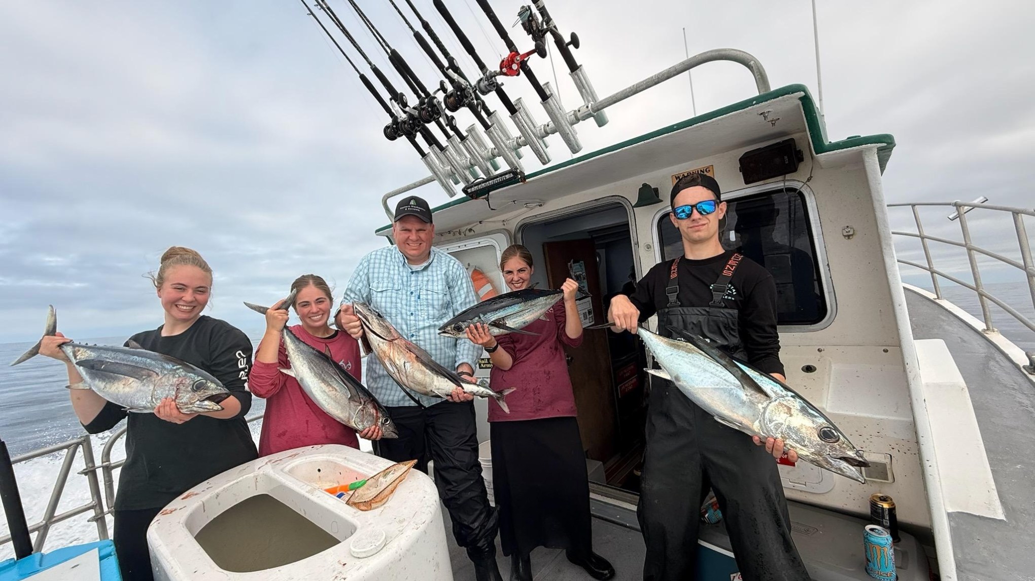 Five people on a boat holding large fish, smiling at the camera.