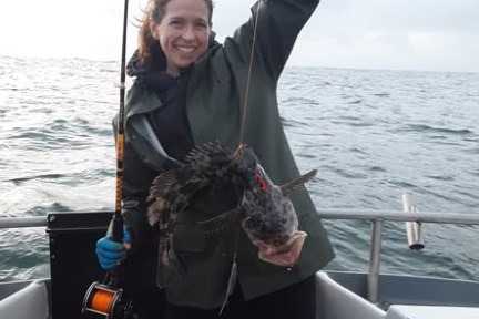Person on boat holding a fishing rod with a caught fish, smiling at the camera.