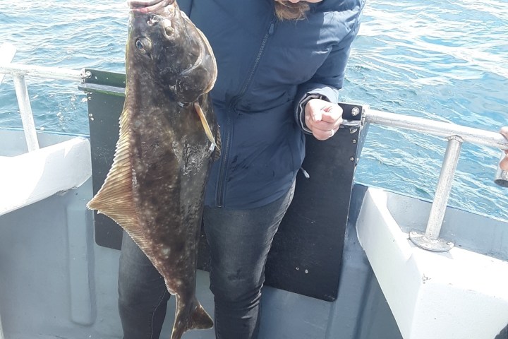 Person holding a large fish on a boat with an ocean background.