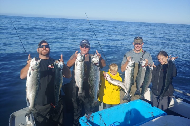 Five people on a boat holding freshly caught fish under a clear blue sky.