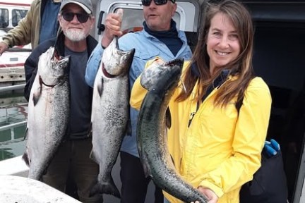 Three people on a boat holding freshly caught large fish and smiling at the camera.