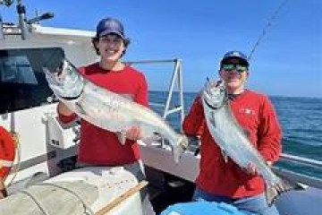 Two people holding large fish on a boat under a clear sky.