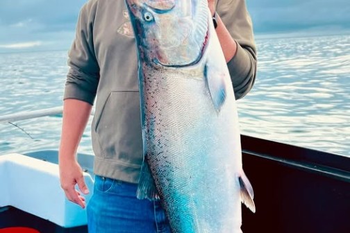 Person on a boat holding a large fish with a cloudy sky and water in the background.