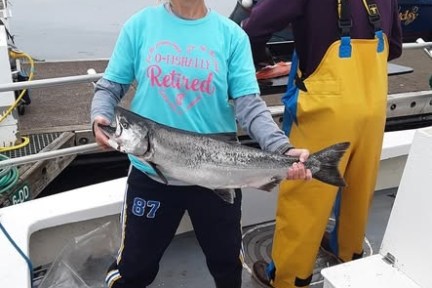 Person on a boat holding a large fish, smiling, wearing a beanie and a 'Retired' T-shirt.