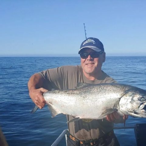 Man holding a large fish on a boat, while someone takes a photo with a smartphone.