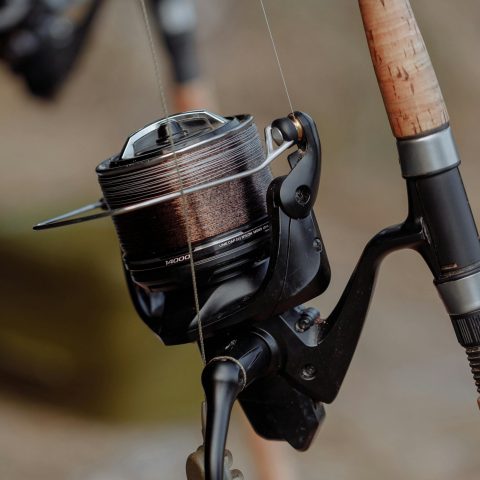 Close-up of a fishing reel and rod with a cork handle, blurred background.